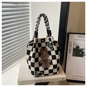 Close-up of knit checkered tote bag with cute rabbit heart patch on a book surface