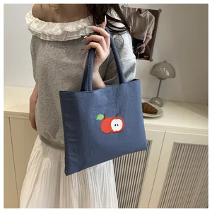 Detail of navy canvas tote bag featuring red apple embroidery with soft handle straps