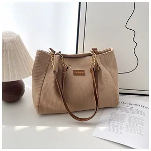 Detail of beige corduroy tote showing texture, leather patch and gold chain strap