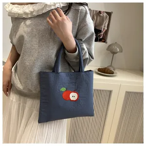 Detail of navy canvas tote bag featuring high-quality red apple embroidery on the front