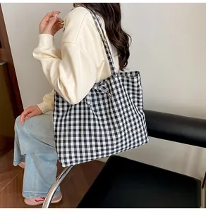 Detailed side view of a black and white gingham tote bag with wide straps on a model