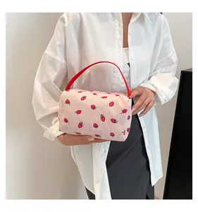 Detail of pink corduroy pouch with strawberry prints held by a hand in soft light