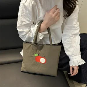 Olive green canvas tote bag with red apple embroidery shown on a model