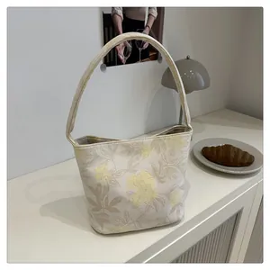 Detail of embroidered floral patterns on an off-white canvas bucket bag for women