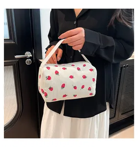 Close-up of a floral corduroy pouch with red strawberry print and white woven handle