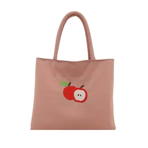 Pink canvas tote bag with embroidered red apple design and thick shoulder straps
