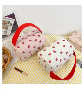 Detail view of corduroy pouches with strawberry patterns and red nylon handles on desk