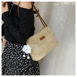 Detail of woven straw tote bag with brown leather straps and white cloud pendant charm
