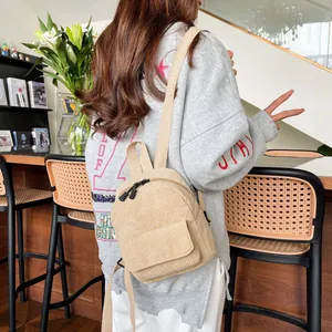 Detailed back view of a beige corduroy mini backpack worn by a model in a cozy interior