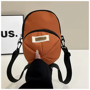 Detail of an orange nylon mini crossbody bag showing textured fabric and black zipper