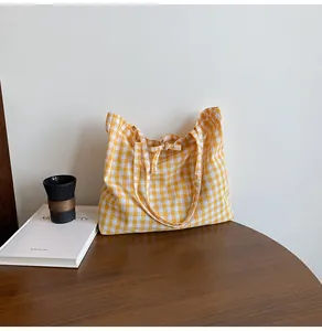 Detail of yellow gingham tote bag with bow tie closure on a dark wooden table