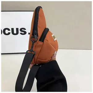 Detail view of orange nylon crossbody bag showing side thickness and double zippers