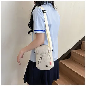 Petit sac bandoulière en nylon beige porté par un mannequin pour un usage quotidien