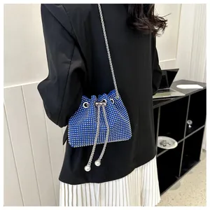 Blauwe bucket bag met strass-steentjes en kettingriem bij een moderne outfit