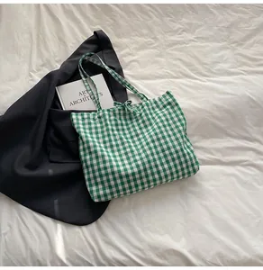 Flat lay of a green gingham canvas tote bag with ribbon bow on white bedding