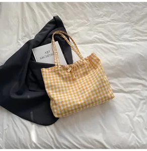 Detail of a yellow gingham canvas tote bag with a small bow knot on a white bed sheet