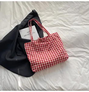 Detail of red and white checkered canvas tote bag with ribbon tie on white linen