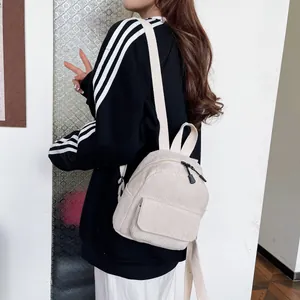 Detailed side view of a cream corduroy mini backpack worn by a model in a casual setting