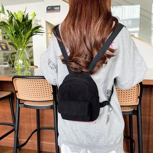 Close-up of a black corduroy mini backpack on a model in a cafe setting