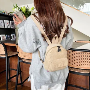 Close-up of a beige corduroy mini backpack worn by a model in a bright café setting