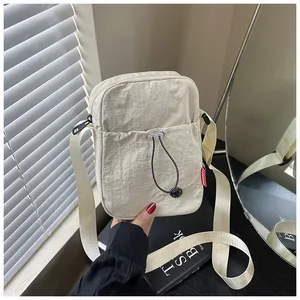 Détail du sac bandoulière en nylon beige avec fermeture noire et poche à cordon