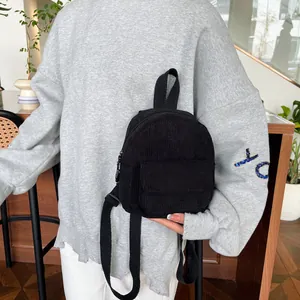 Detailed view of mini black corduroy backpack held by model for size reference