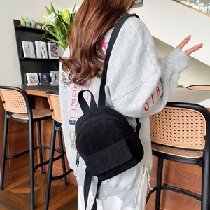 Detailed close-up of a mini black corduroy backpack on a person in a cozy cafe setting
