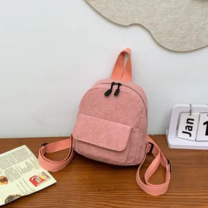 Close-up of pink corduroy mini backpack on wooden table with dual zippers and front pocket