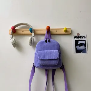 Detail of purple corduroy mini backpack hanging on wooden rack with fabric straps