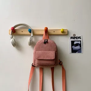Detail of pink corduroy mini backpack with contrast coral straps on a wooden hook
