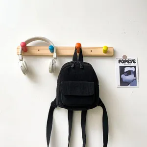 Close-up of black corduroy mini backpack hanging on a hook with lifestyle props