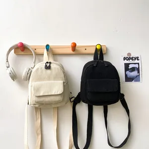 Detailed corduroy texture of mini backpacks in cream and black hanging on wall hooks