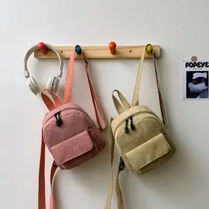 Detailed texture of pink and beige mini corduroy backpacks hanging on wooden hooks