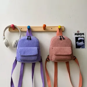 Detail view of purple and pink corduroy mini backpacks hanging on wall hooks