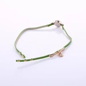 Detail of green leather strap with gold clasp and sparkling rhinestone charm on watch