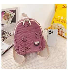Detail of purple corduroy mini backpack with smiley face next to a smartphone