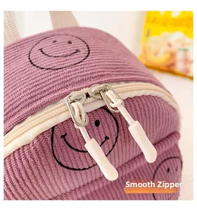 Detail view of smooth double zippers on purple corduroy bag with embroidered smiley face