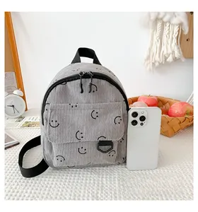 Detailed macro view of grey corduroy backpack with smiley face next to a smartphone