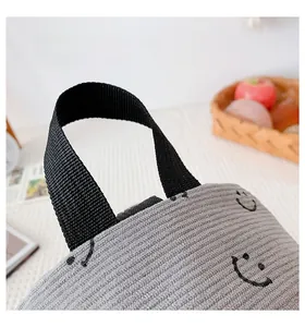 Detail of grey corduroy bag featuring a black nylon handle and smiley face embroidery