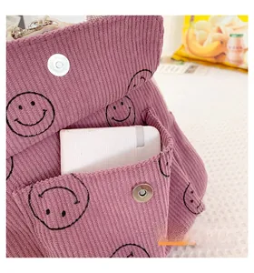 Detail of pink corduroy backpack featuring black smiley faces and magnetic metal buckle