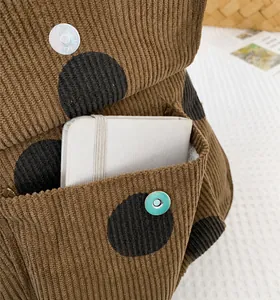 Detail of brown corduroy polka dot mini backpack featuring a front pocket with magnetic snap