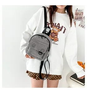 Detail of gray corduroy mini backpack with black smiley embroidery on a model