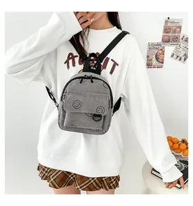 Close-up of grey corduroy mini backpack with black smiley face worn as a chest bag