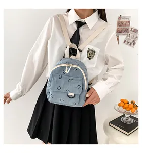 Detail of light blue corduroy mini backpack featuring a smiley face pattern and adjustable straps