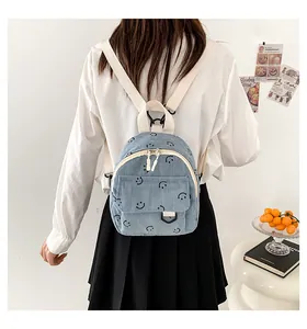 Detailed close-up of light blue corduroy backpack with smiley prints and cream straps