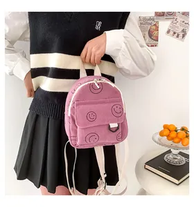 Detail of pink corduroy backpack with smiley face pattern held by model in casual setting