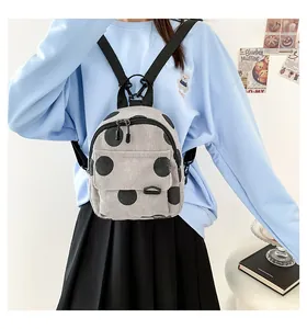 Detail view of light grey corduroy mini backpack with black polka dots on model