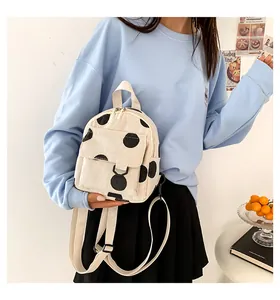 Close-up of beige corduroy mini backpack with black polka dots on a model wearing blue