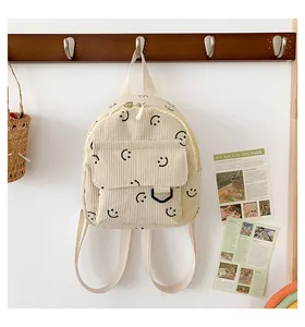 Detail of beige corduroy backpack featuring repeat black smiley face patterns and texture