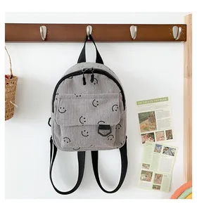 Detail view of grey corduroy backpack with black smile face patterns hanging on a wooden hook